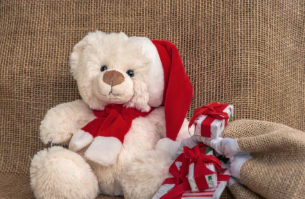 A 4K Ultra HD desktop wallpaper featuring a white teddy bear wearing a Santa hat and red scarf, holding holiday gifts wrapped in burlap and red ribbons.