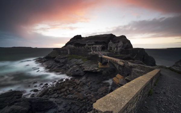 Sunset over a ruined coastal fort and man-made stone bridge at Saint-Malo, Brittany, France — rocky shore and moody skies, HD desktop wallpaper.