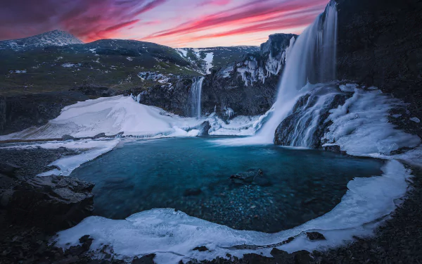 Skógafoss waterfall in Iceland at sunset, surrounded by icy river and snow-covered mountains, captured in a vibrant HD desktop wallpaper.