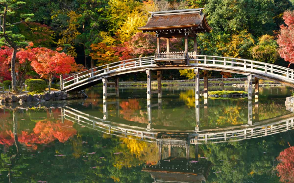 A man-made gazebo and curved bridge reflect beautifully on a serene park pond, surrounded by vibrant fall foliage in this 4K Ultra HD desktop wallpaper.