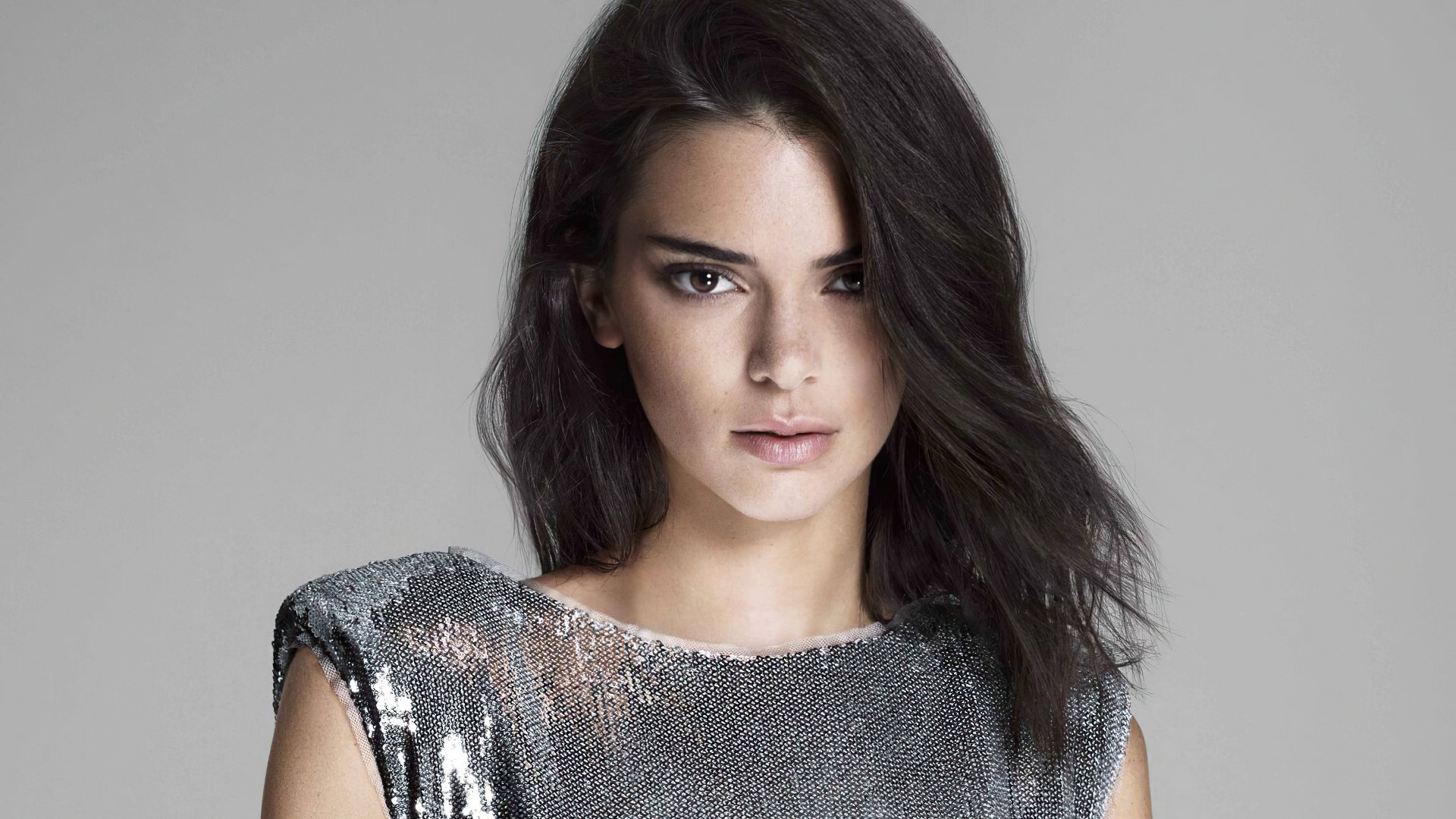 Studio portrait of a female celebrity model with long black hair wearing a silver sequined top, polished 4K desktop wallpaper background.