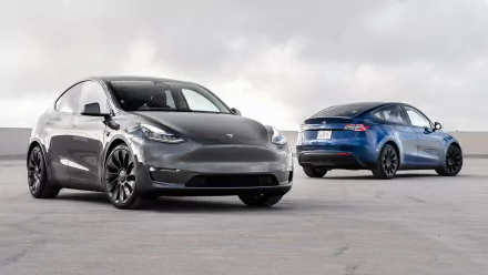HD wallpaper featuring two Tesla Model Y electric cars, one in gray and the other in blue, positioned on a cloudy day.