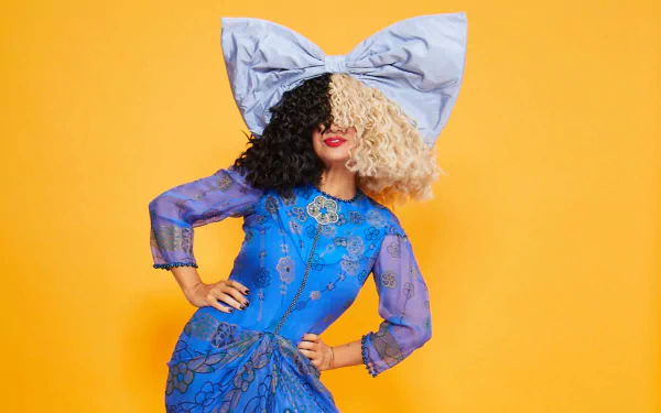 A person with a large bow headpiece and two-toned hair posing against a vibrant orange background, suitable as a HD desktop wallpaper.