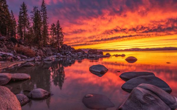 Sunset over Lake Tahoe in Nevada, USA, with vibrant orange and purple skies reflecting on the calm water, surrounded by rocky shores and pine trees.