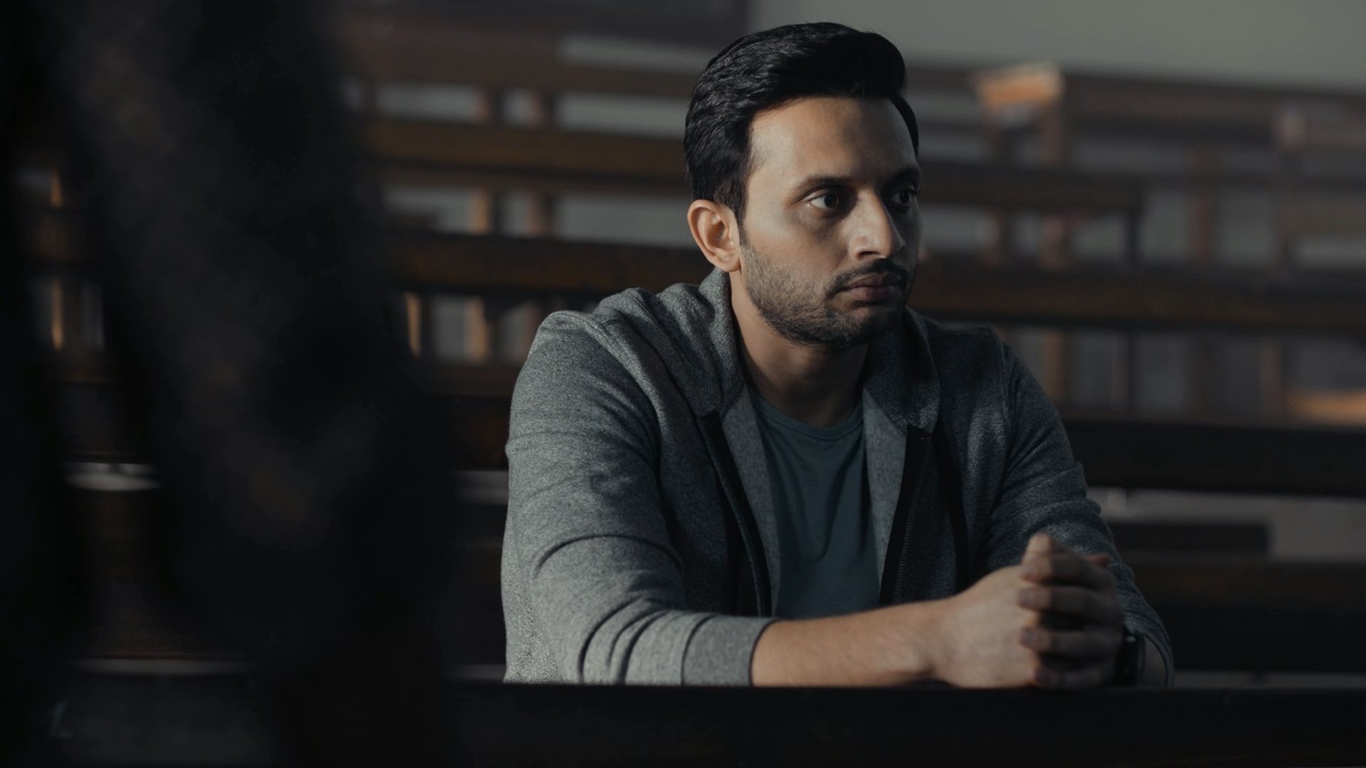 HD desktop wallpaper featuring a contemplative person from Tandav, set in a dimly lit room.