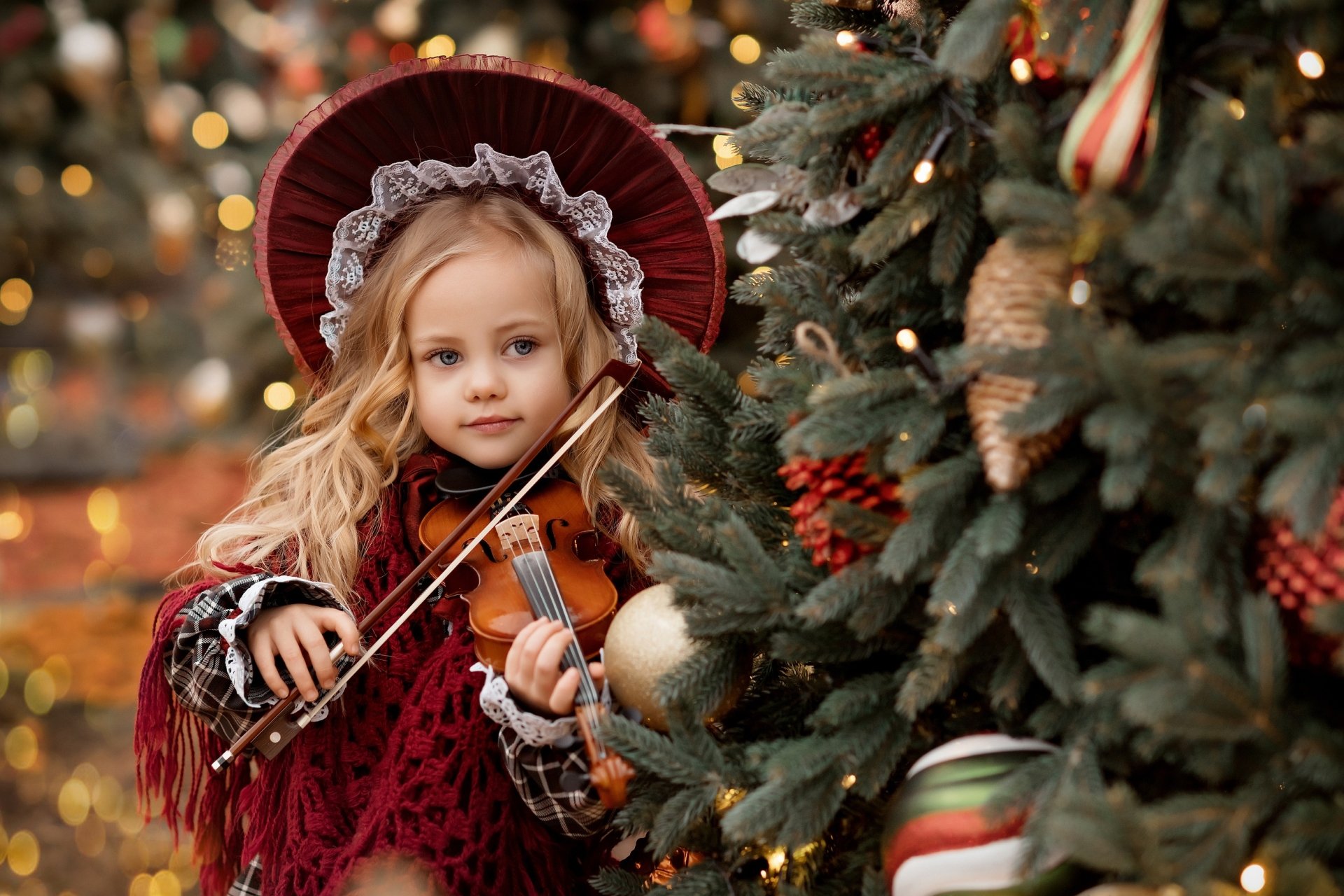 Blonde child wearing a hat plays violin next to a decorated Christmas tree in this HD photography desktop wallpaper.
