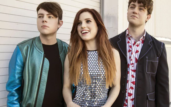 HD wallpaper featuring the band Echosmith with Sydney Sierota in the center, accompanied by two male band members, against a white wall background.