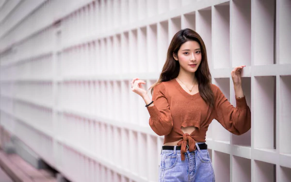 Asian brunette woman posing against a textured wall with depth of field effect, captured in crisp 8K Ultra HD for a PC desktop wallpaper and background.