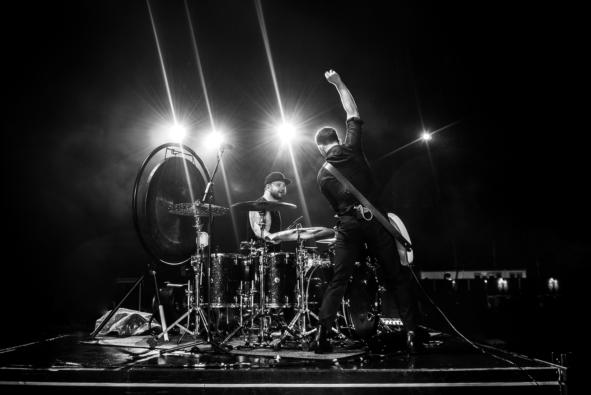 Black and white HD desktop wallpaper featuring a dynamic concert scene with a guitarist and a drummer performing energetically under bright stage lights, tagged with Royal Blood.