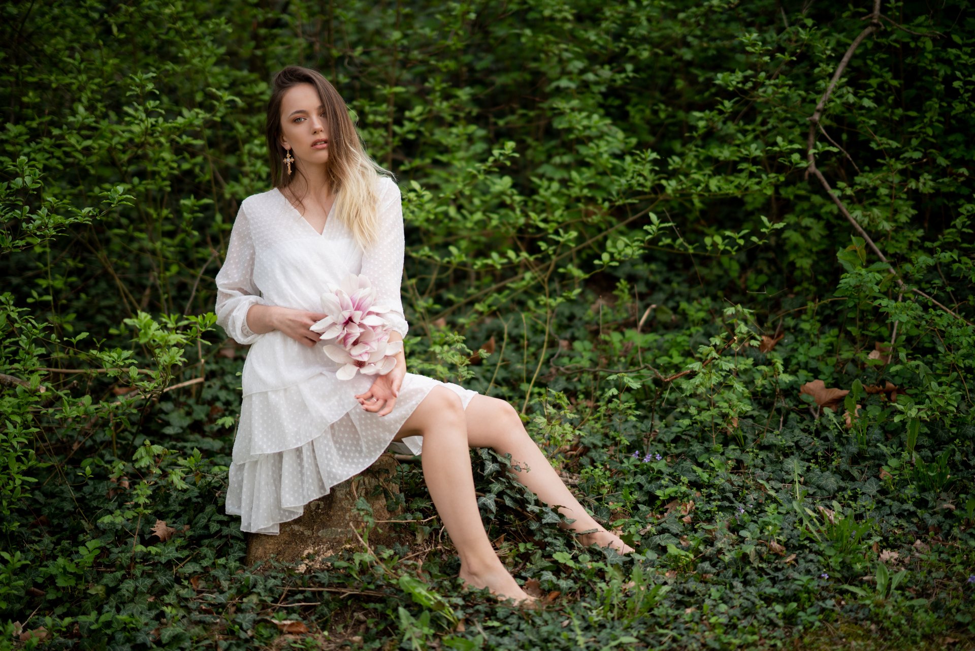 Brunette woman in a white dress sits on greenery, holding flowers, captured in a 4K Ultra HD PC desktop wallpaper featuring a natural, serene outdoor setting.