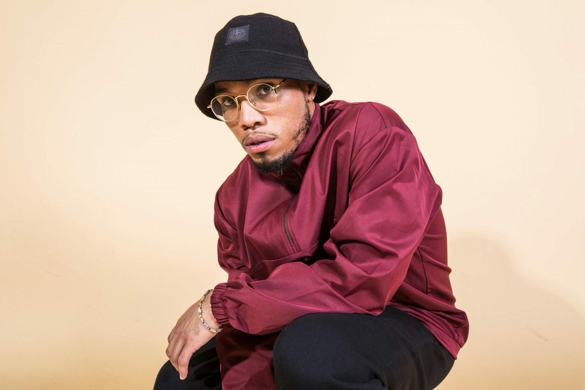 HD desktop wallpaper featuring Anderson .Paak in a maroon outfit and black hat against a beige background.