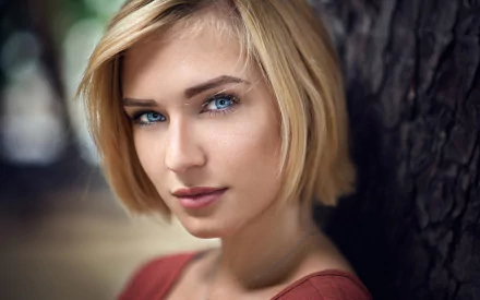 Close-up of Eva Mikulski, a blonde woman with short hair and striking blue eyes, posing outdoors against a blurred natural background in this HD desktop wallpaper.