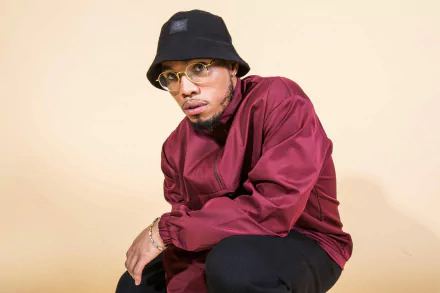 HD desktop wallpaper featuring Anderson .Paak in a maroon outfit and black hat against a beige background.