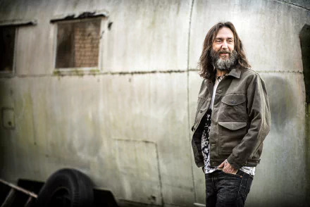Chris Robinson of The Black Crowes poses with a smile against a weathered backdrop for an HD desktop wallpaper.