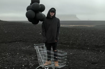 Person standing on a desolate terrain with a shopping cart and black balloons, moody HD wallpaper.
