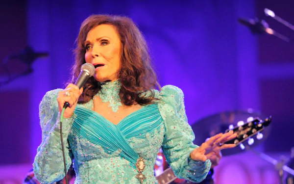 HD wallpaper featuring a woman in a teal dress singing into a microphone, with a guitar player in the background.