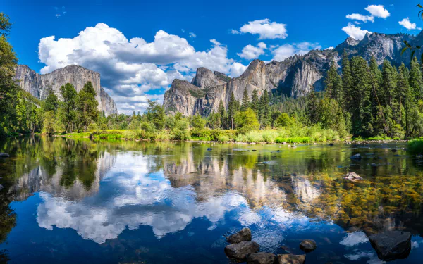 HD desktop wallpaper of Yosemite National Park, USA, showcasing a stunning mountain landscape with a crystal-clear lake, reflecting the surrounding nature under a bright blue sky with fluffy clouds.
