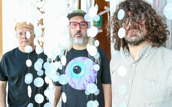 HD wallpaper featuring three members of the band Dinosaur Jr. standing in front of a decorative hanging backdrop.