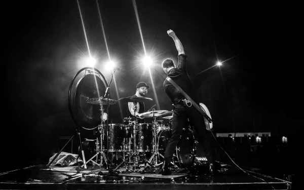 Black and white HD desktop wallpaper featuring a dynamic concert scene with a guitarist and a drummer performing energetically under bright stage lights, tagged with Royal Blood.