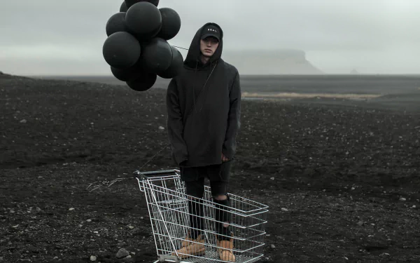 Person standing on a desolate terrain with a shopping cart and black balloons, moody HD wallpaper.