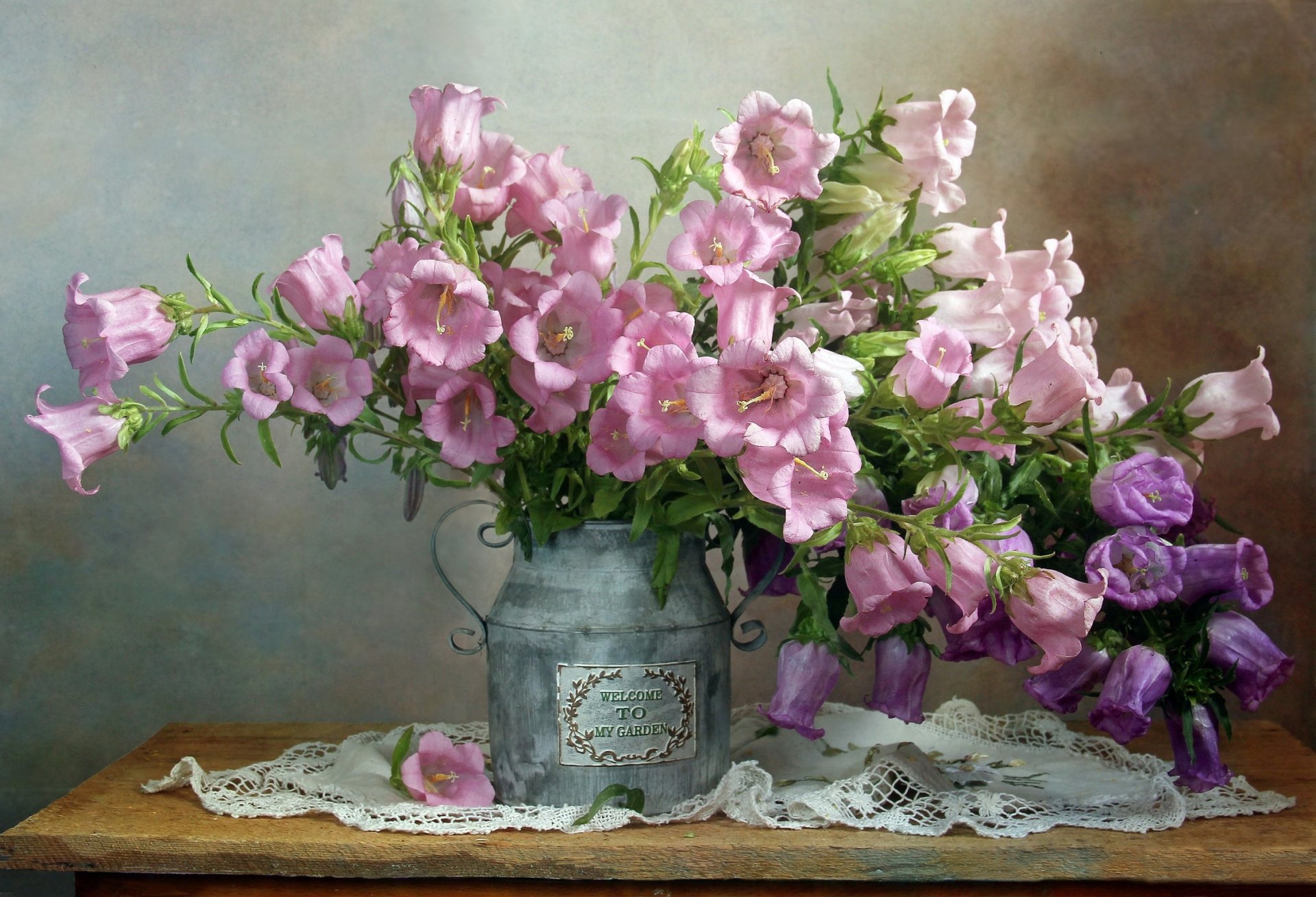 HD still life photography of a bouquet of pink and purple flowers arranged in a rustic metal vase on a lace-covered wooden table, captured as a PC desktop wallpaper.