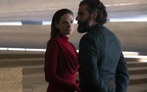 Two characters from the movie Dune (2021) — a bearded man and a woman in red — stand in a sleek sci‑fi hall. HD PC desktop wallpaper/background.