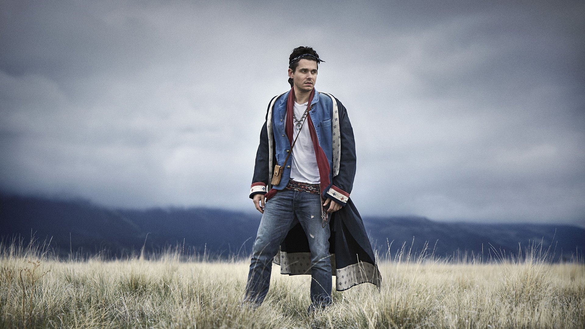 HD desktop wallpaper featuring a man in stylish attire standing in a field with stormy skies overhead.