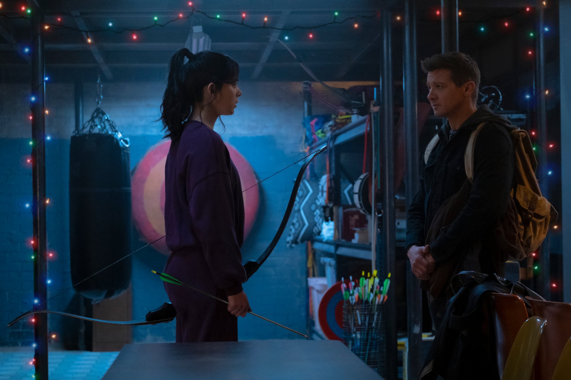 HD PC desktop wallpaper featuring Clint Barton and Kate Bishop from the Hawkeye TV show, portrayed by Jeremy Renner and Hailee Steinfeld, in a dimly lit room with archery gear.