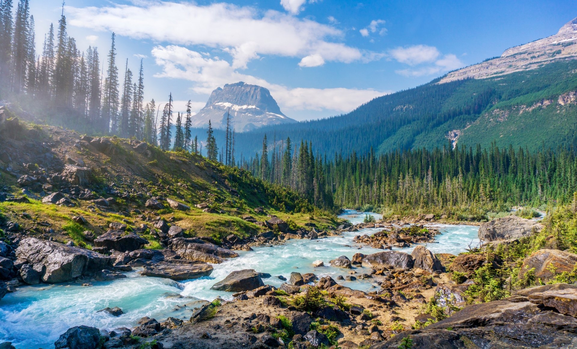 A 4K Ultra HD desktop wallpaper showcasing a vibrant mountain landscape with a flowing river, dense forest, and clear blue sky in a pristine natural setting.
