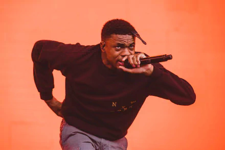 HD desktop wallpaper featuring a dynamic performance shot of Vince Staples with a microphone against an orange backdrop.