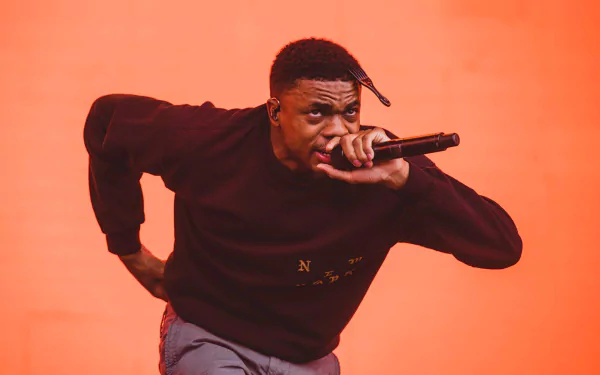 HD desktop wallpaper featuring a dynamic performance shot of Vince Staples with a microphone against an orange backdrop.