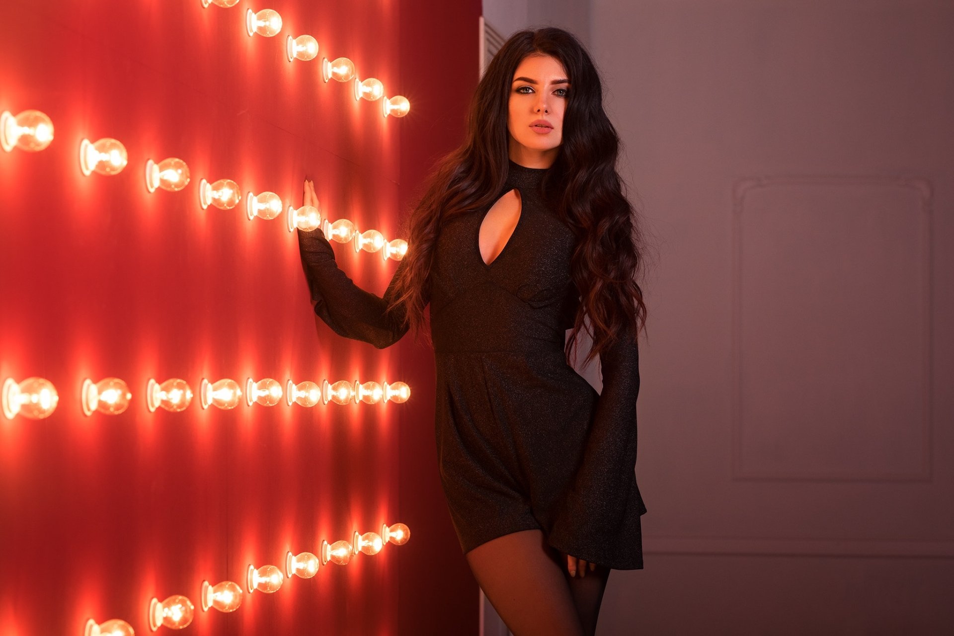HD desktop wallpaper of a model with long black hair wearing a black dress, posing against a wall lined with glowing round lights.