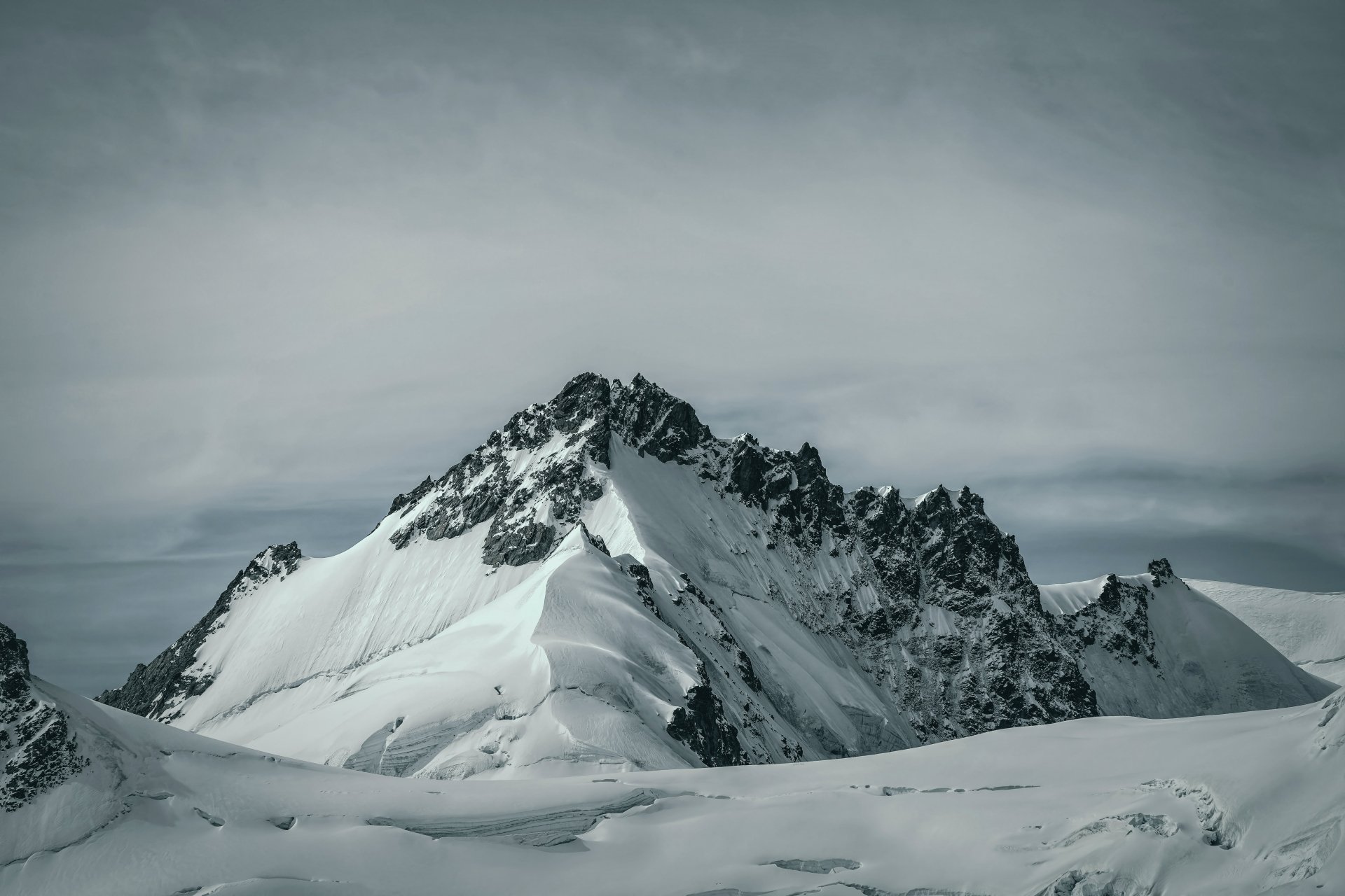 Snow-covered mountain peaks under a cloudy sky, captured in stunning 4K Ultra HD, showcasing the serene beauty of winter nature.