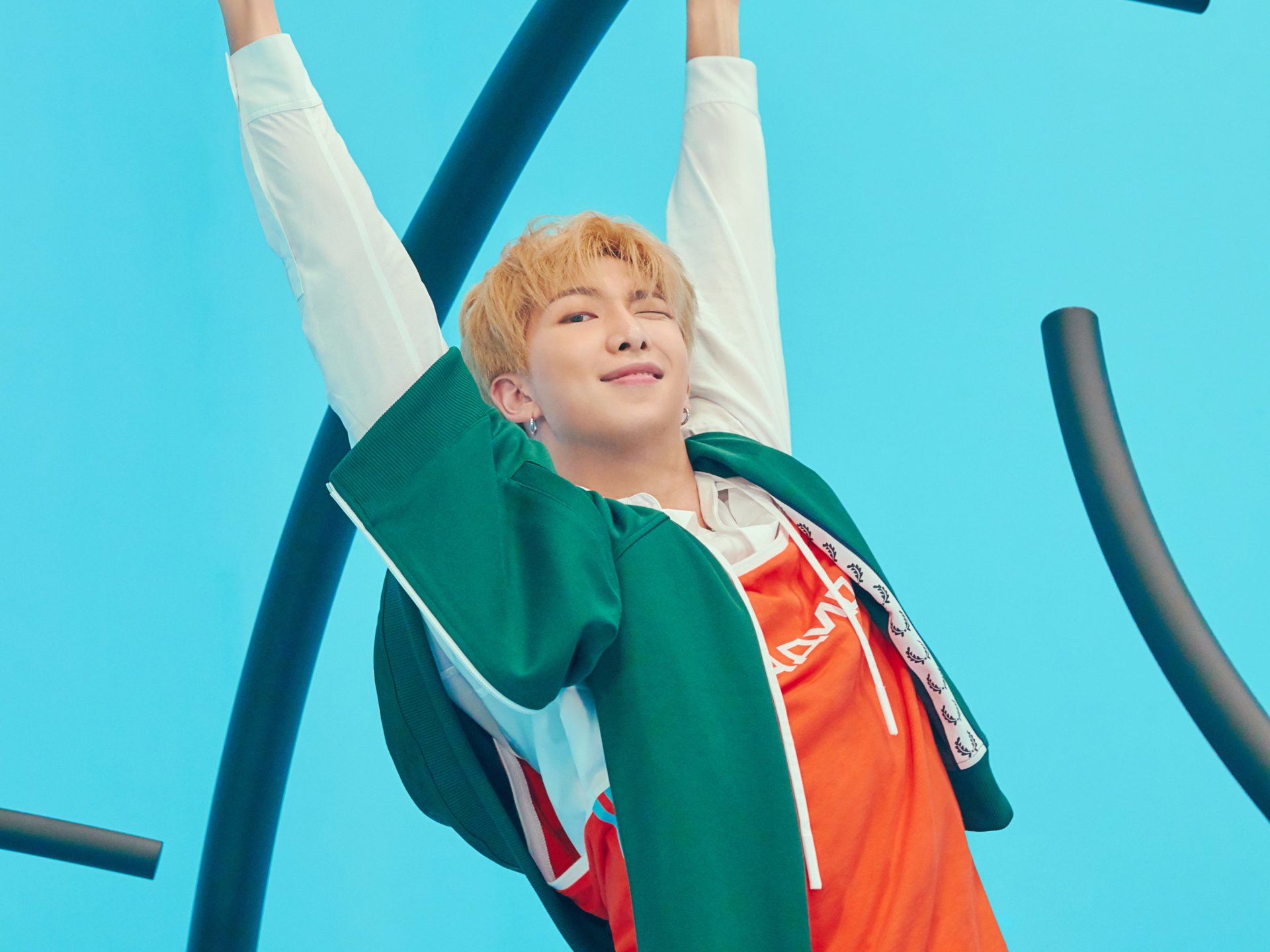 HD desktop wallpaper of RM (Kim Namjoon) from BTS, a K-pop singer, smiling with arms raised against a bright blue sky background.