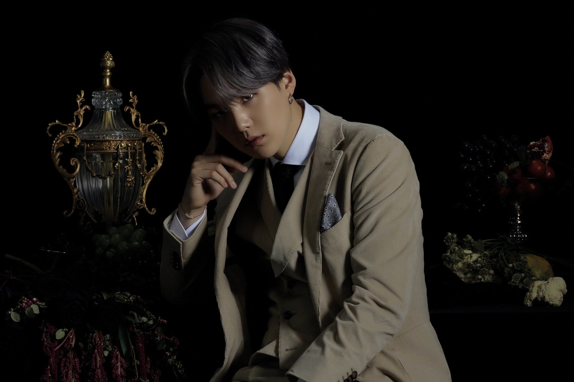 HD desktop wallpaper of Suga (Min Yoongi) from BTS, the K-pop singer, dressed in a beige suit against a dark, ornate background.
