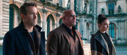 2K Quad HD PC desktop wallpaper of three actors—two men and a woman—standing in coats before an ornate historic building, cinematic framing and serious expressions.