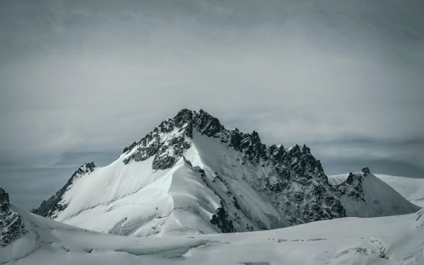 Snow-covered mountain peaks under a cloudy sky, captured in stunning 4K Ultra HD, showcasing the serene beauty of winter nature.