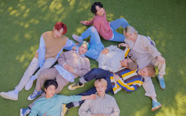 A vibrant HD wallpaper featuring the K-pop group ATEEZ, showcasing the members joyfully posed on green grass, radiating energy and camaraderie in a sunny setting.