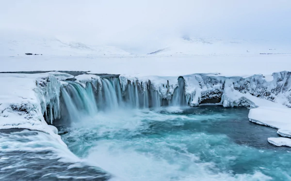 4K Ultra HD image of Iceland’s Goðafoss waterfall surrounded by snow and icy terrain, showcasing pristine nature in a serene winter landscape.