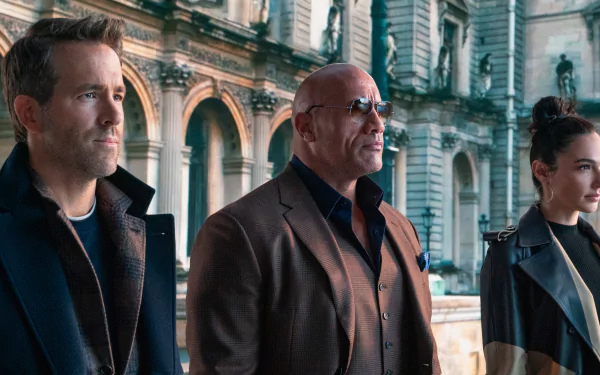 2K Quad HD PC desktop wallpaper of three actors—two men and a woman—standing in coats before an ornate historic building, cinematic framing and serious expressions.