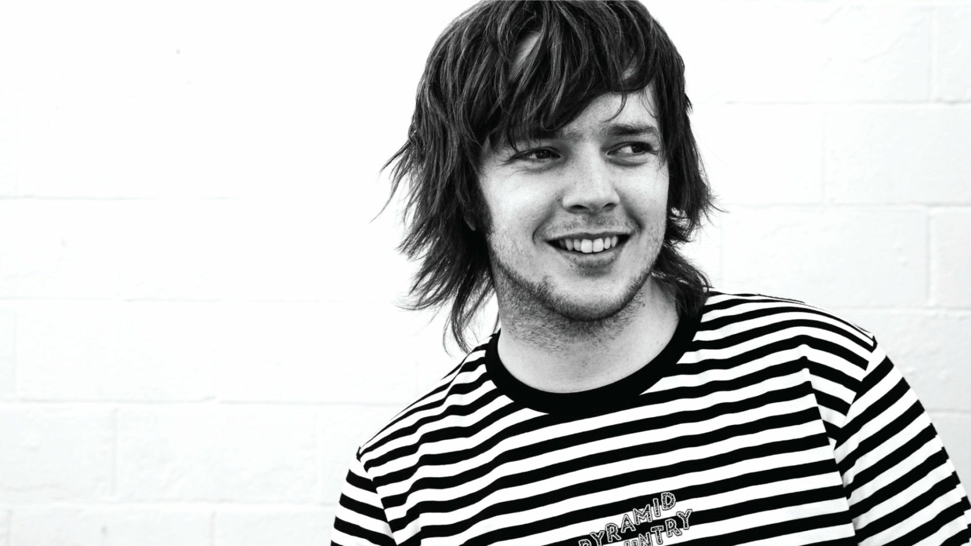 HD desktop wallpaper featuring a smiling man with shaggy hair wearing a striped shirt against a plain background, tagged as Billy Strings.