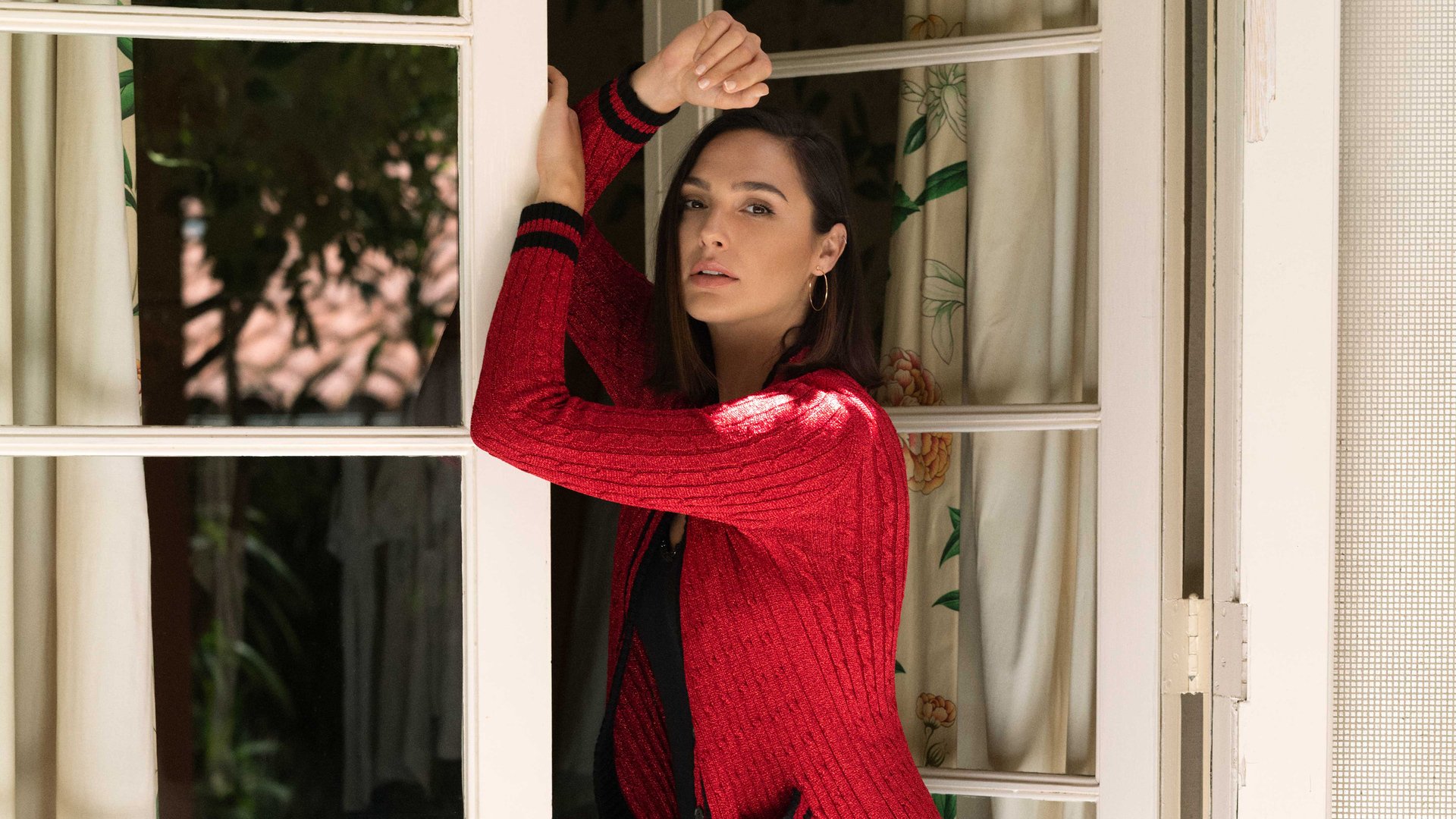 HD PC desktop wallpaper featuring celebrity Gal Gadot posing thoughtfully by a window in a red sweater.