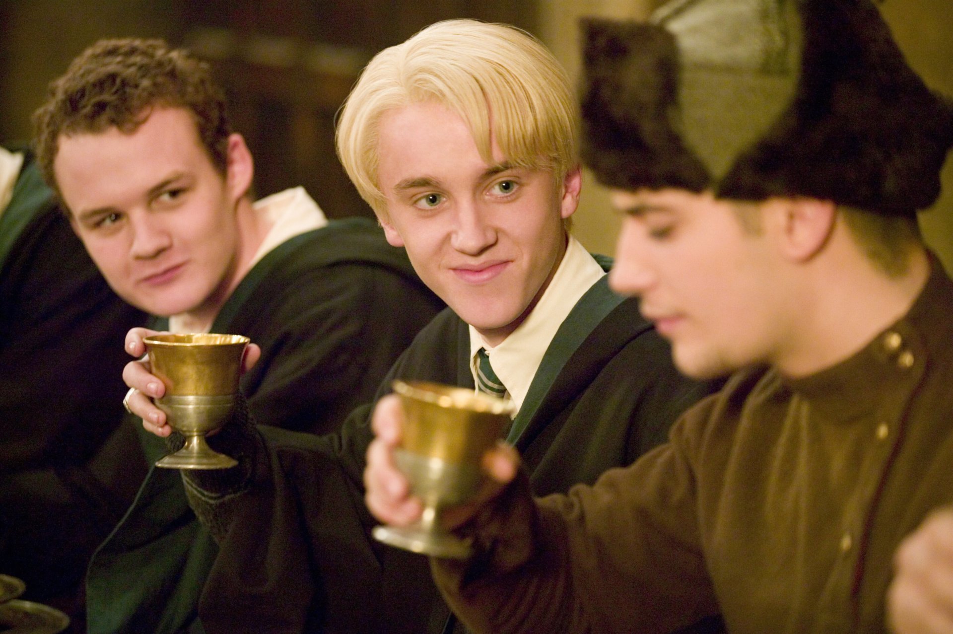 HD PC desktop wallpaper: Draco Malfoy, Gregory Goyle, and Viktor Krum raising goblets in a Hogwarts feast scene from Harry Potter and the Goblet of Fire.