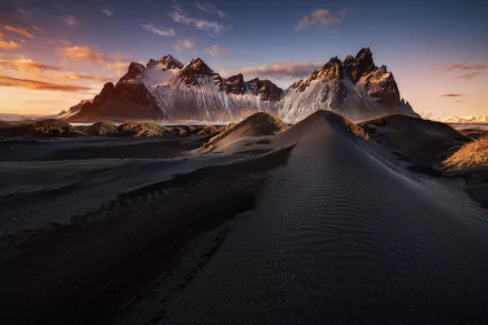 HD desktop wallpaper of Vestrahorn mountain in Iceland, featuring dramatic peaks rising above dark sand dunes under a vibrant sunset sky.