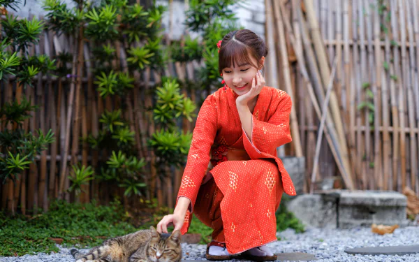Woman in a red kimono crouches to pet a tabby cat in a bamboo garden; 4K Ultra HD PC desktop wallpaper and background.