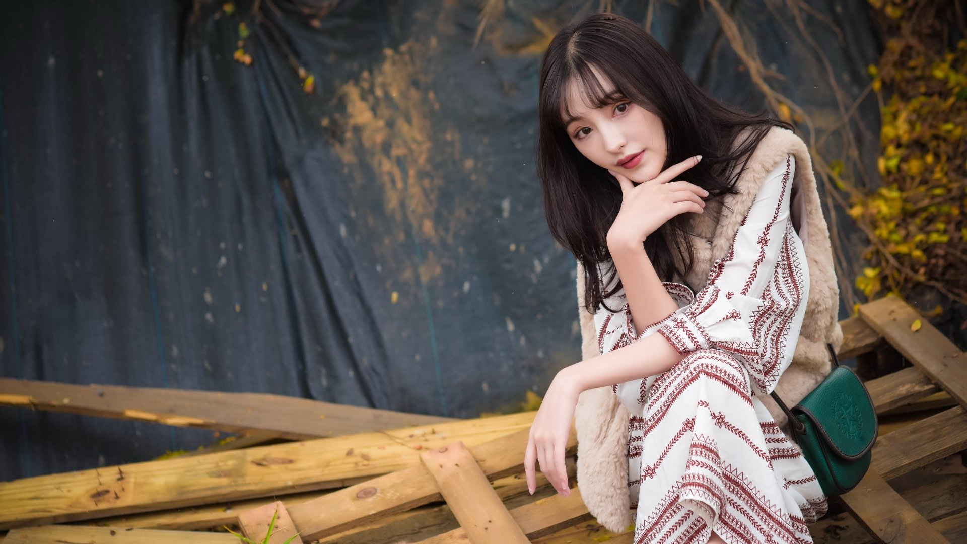 A 4K Ultra HD desktop wallpaper featuring an Asian woman with black hair, dressed in patterned attire, sitting thoughtfully among wooden logs with a dark backdrop.