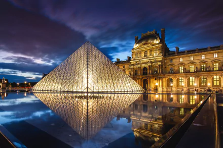 HD desktop wallpaper of The Louvre's glass pyramid and historic museum building reflected in still water at dusk in Paris, dramatic sky and illuminated man-made architecture.