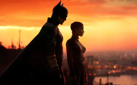 HD desktop wallpaper featuring Batman and Catwoman, portrayed by Zoë Kravitz, from the movie The Batman, standing against a cityscape with a vivid sunset in the background.