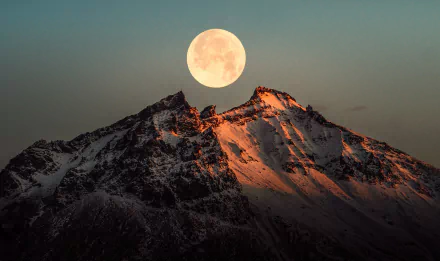 4K Ultra HD wallpaper of a glowing full moon rising over snow-capped Icelandic mountains at dusk, highlighting rugged peaks and serene natural beauty.
