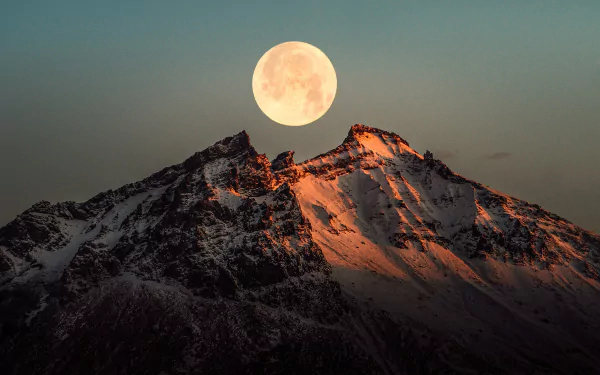 4K Ultra HD wallpaper of a glowing full moon rising over snow-capped Icelandic mountains at dusk, highlighting rugged peaks and serene natural beauty.